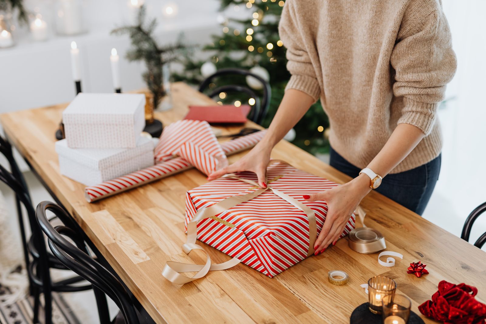 A person wrapping a holiday gift at a table in a real home